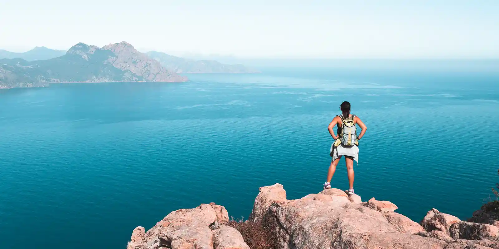 A single hiker on top of a wild peak surveys the view of snow topped mountains in the distance