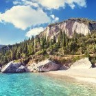 Sandy beach and turquoise sea of Corfu alongside mountain scenery