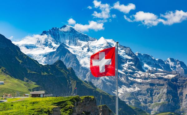 Swiss flag in front of snowy mountain peaks